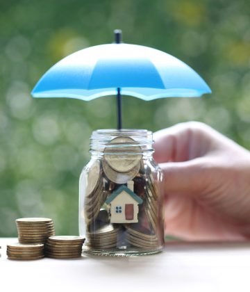 Protection,Model house and gold coin money in the glass bottle with hand holding the umbrella on natural green background, Finance insurance and Safe investment concept